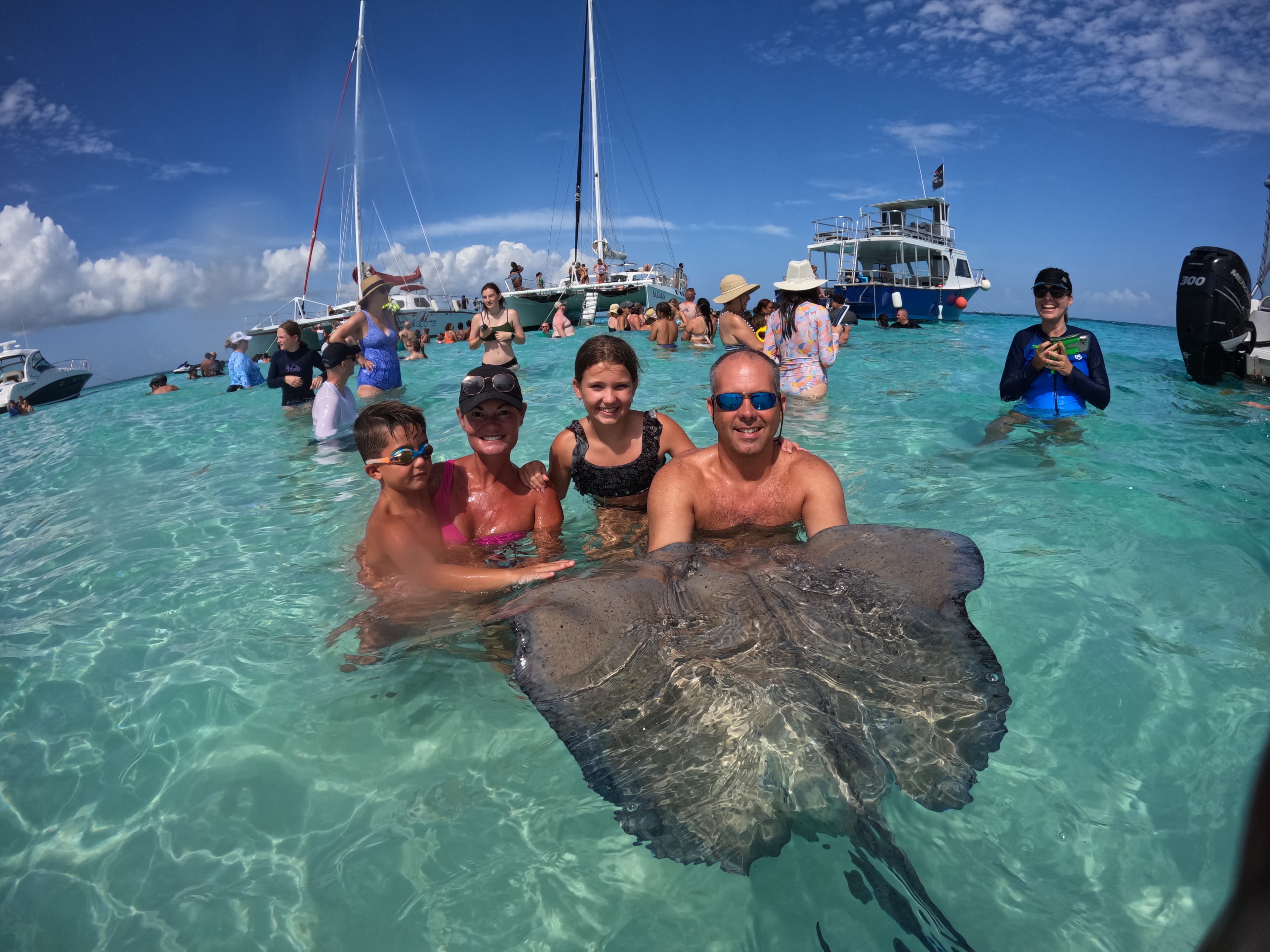 Elizabeth with family and a large sting ray in the ocean with other people and boats surrounding them