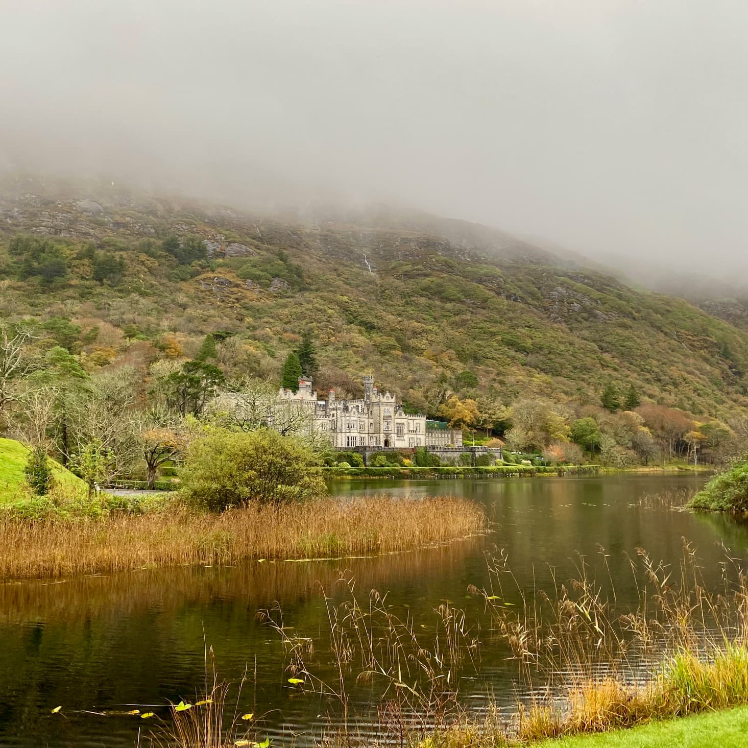 Misty view of a green hill and river with a white castle on a foggy day