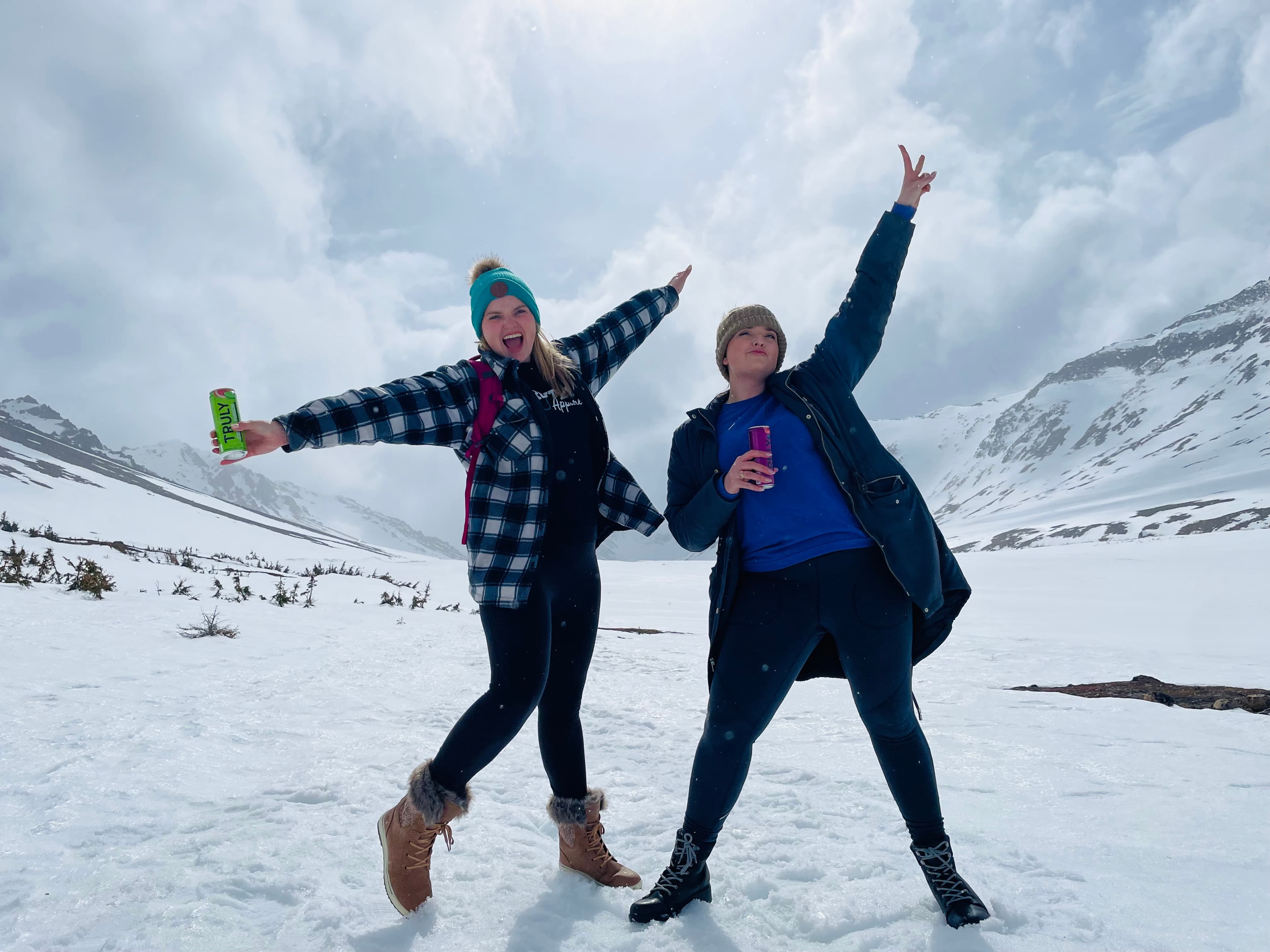 Travel advisor posing in the snow with a female companion wearing a checkered shirt and hat holding a drink