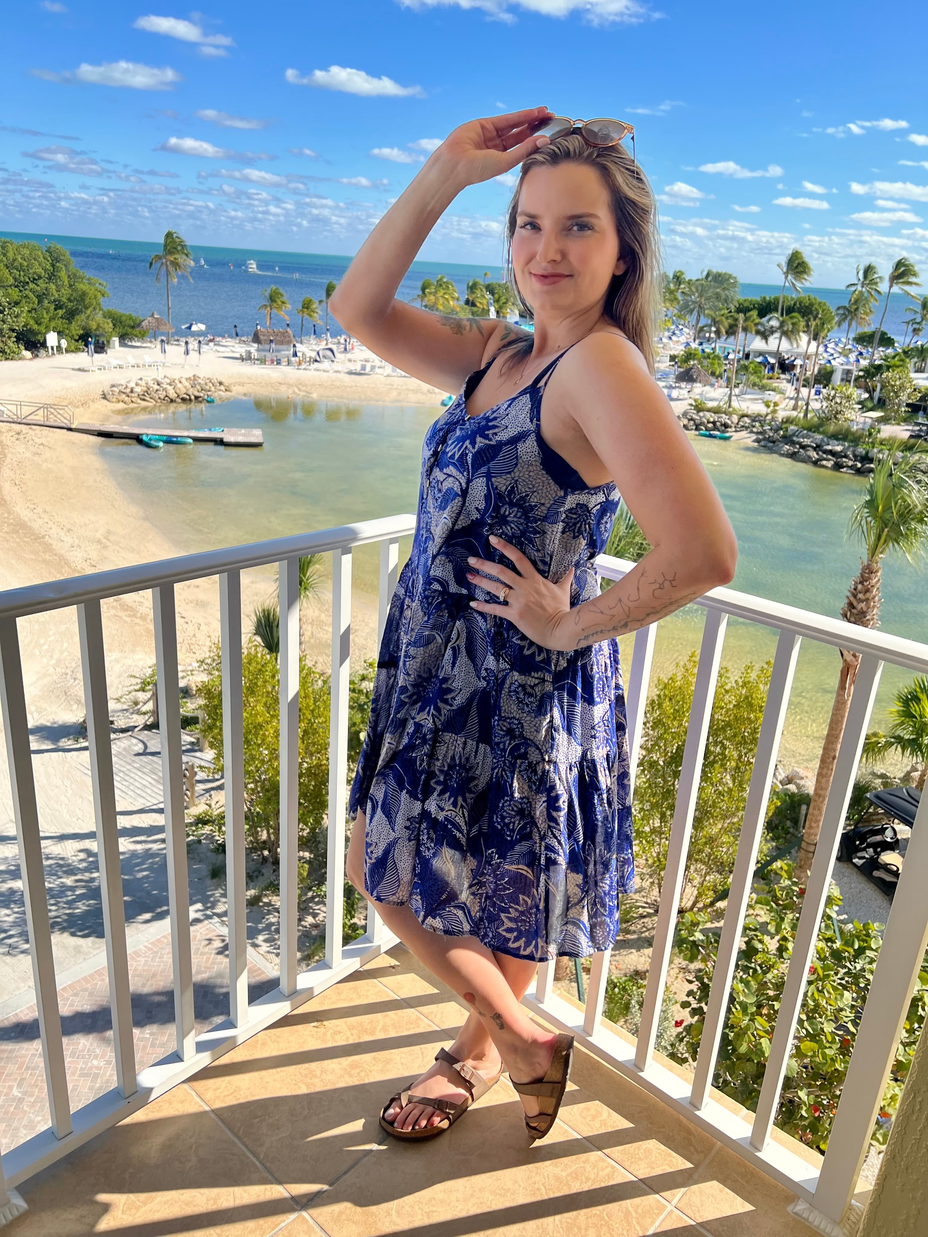 Travel advisor Elizabeth posing on a balcony in a blue and white dress overlooking a beach