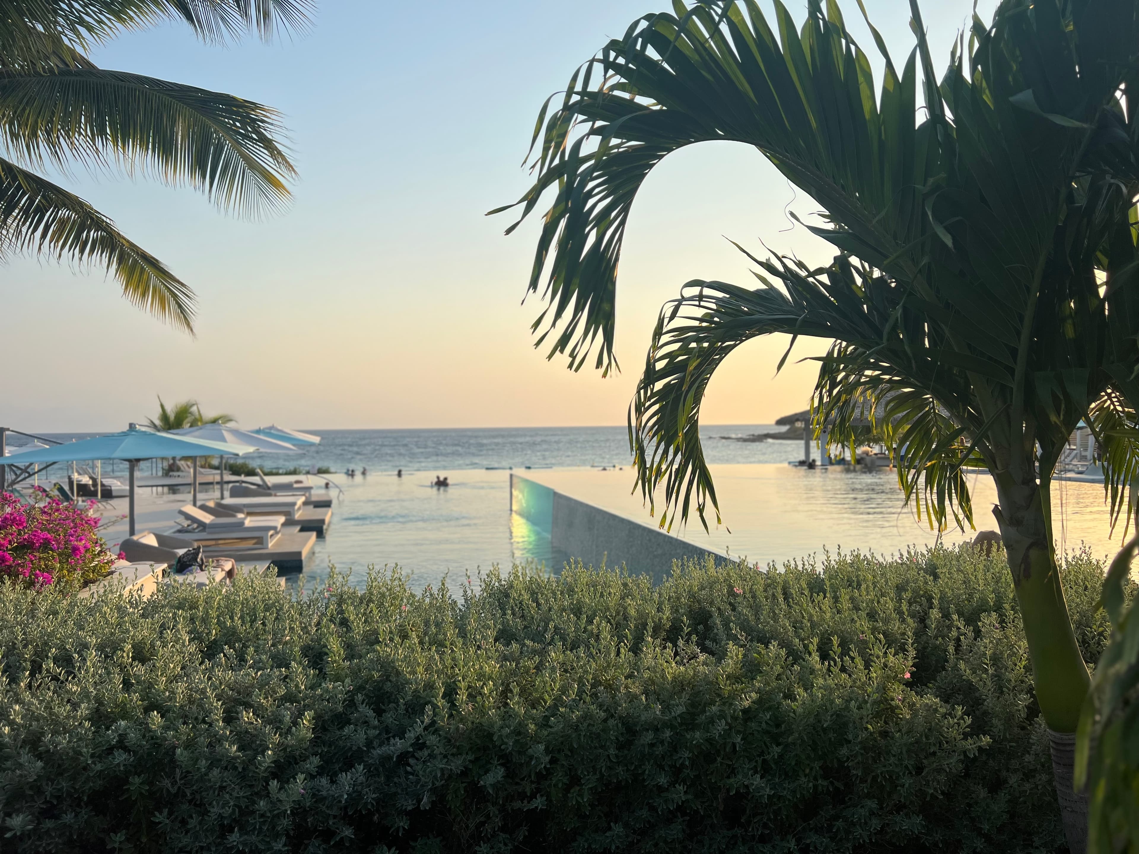 Beautiful view of infinity pool at a resort at sunset with palm trees, loungers and umbrellas