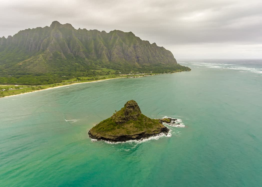 An aerial view of the ocean with a green island in the middle and mountains and green landscape to one side