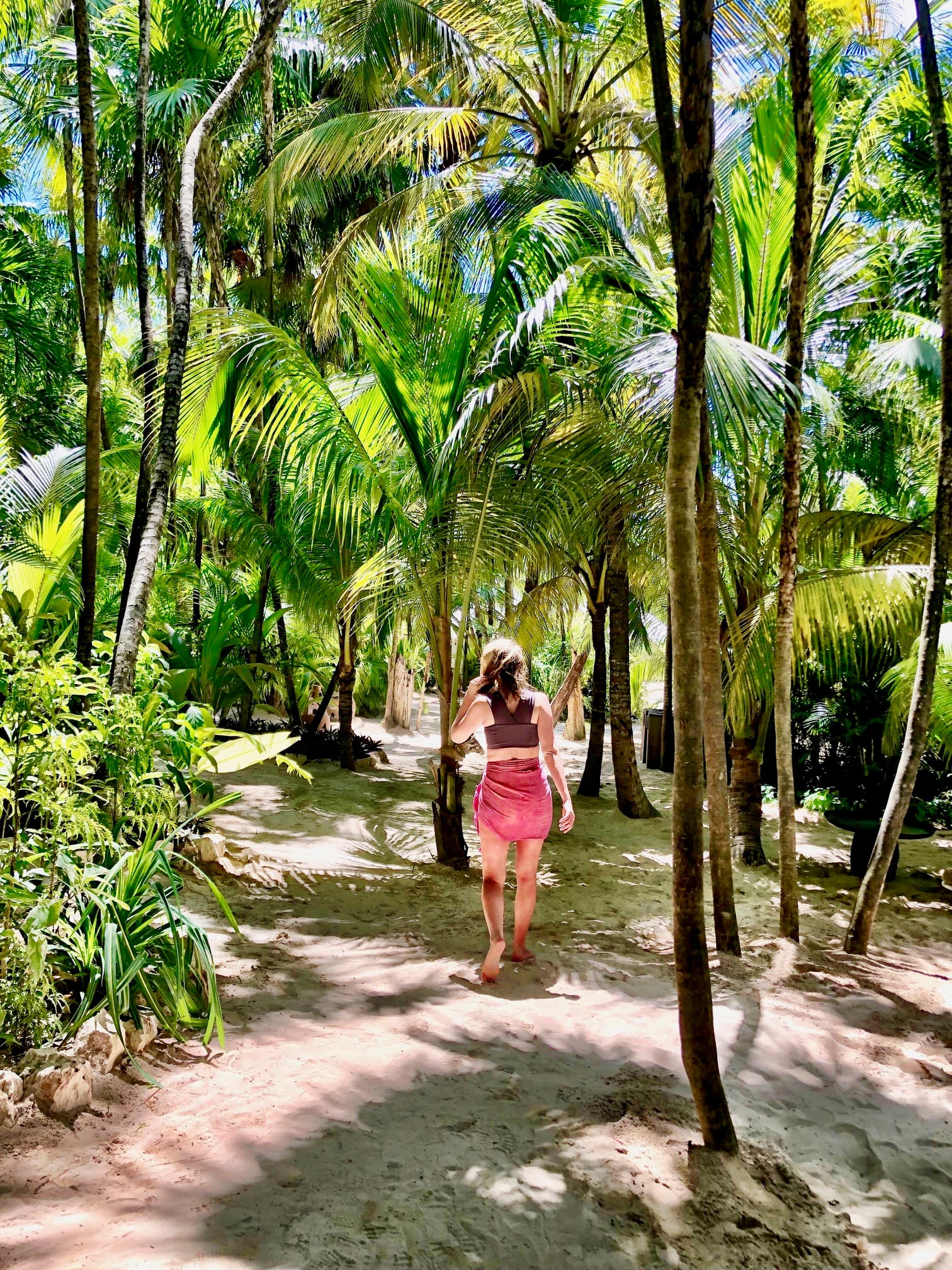 Allison walking down a dirt path surrounding by palm trees on a sunny day.