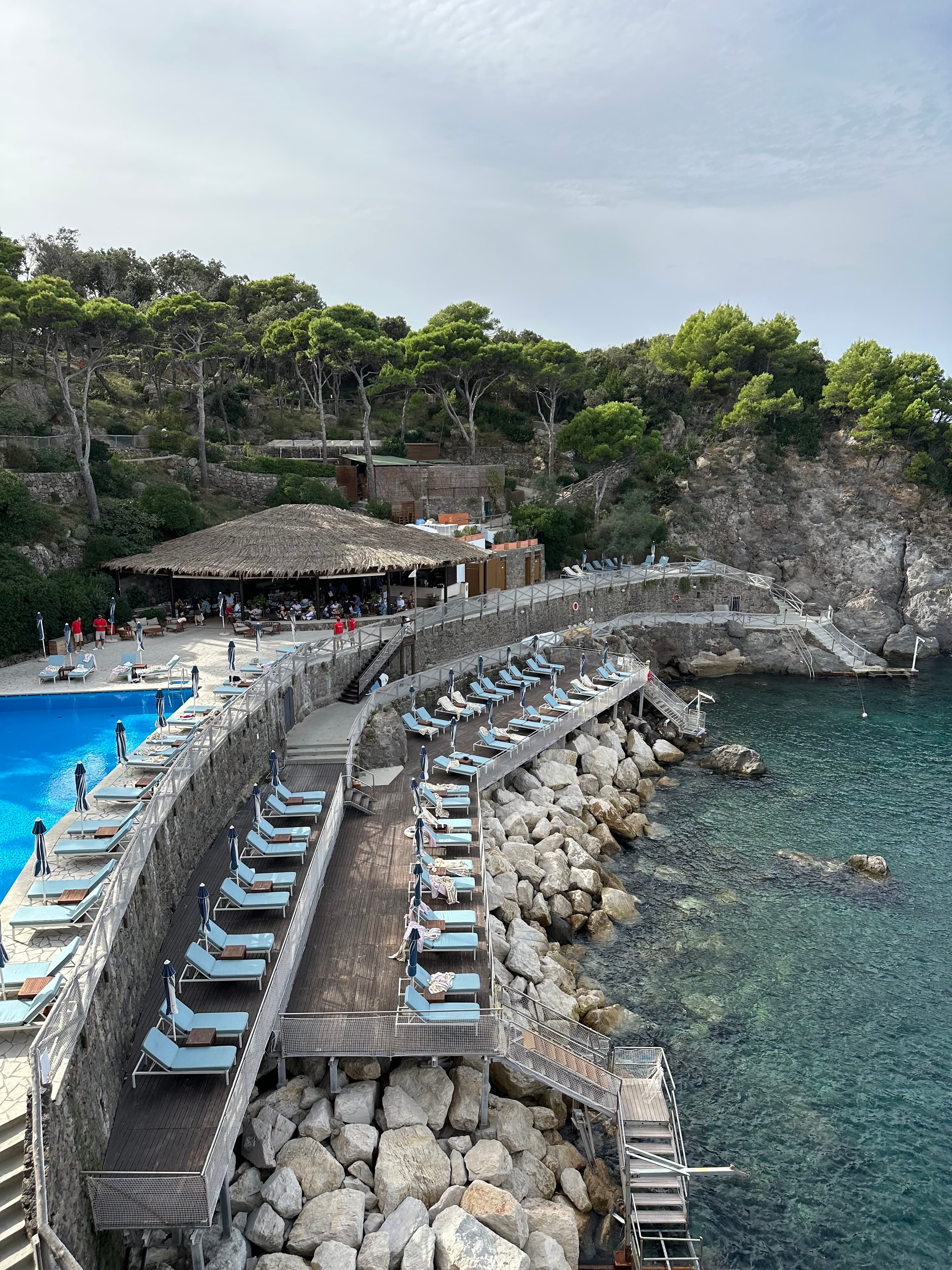 View of hotel pool and loungers on different levels overlooking the ocean