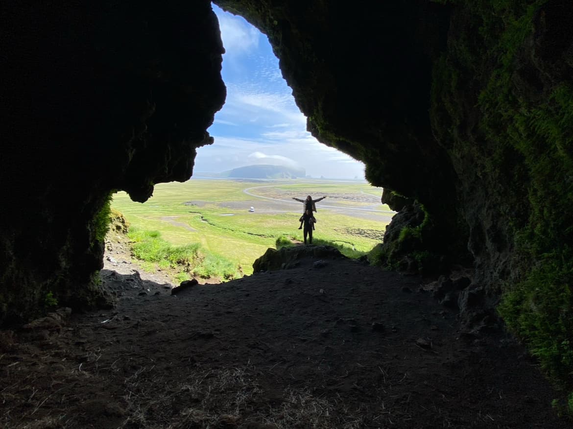 Beautiful view from a cave of green landscape and two people posing at the entrance of the cave