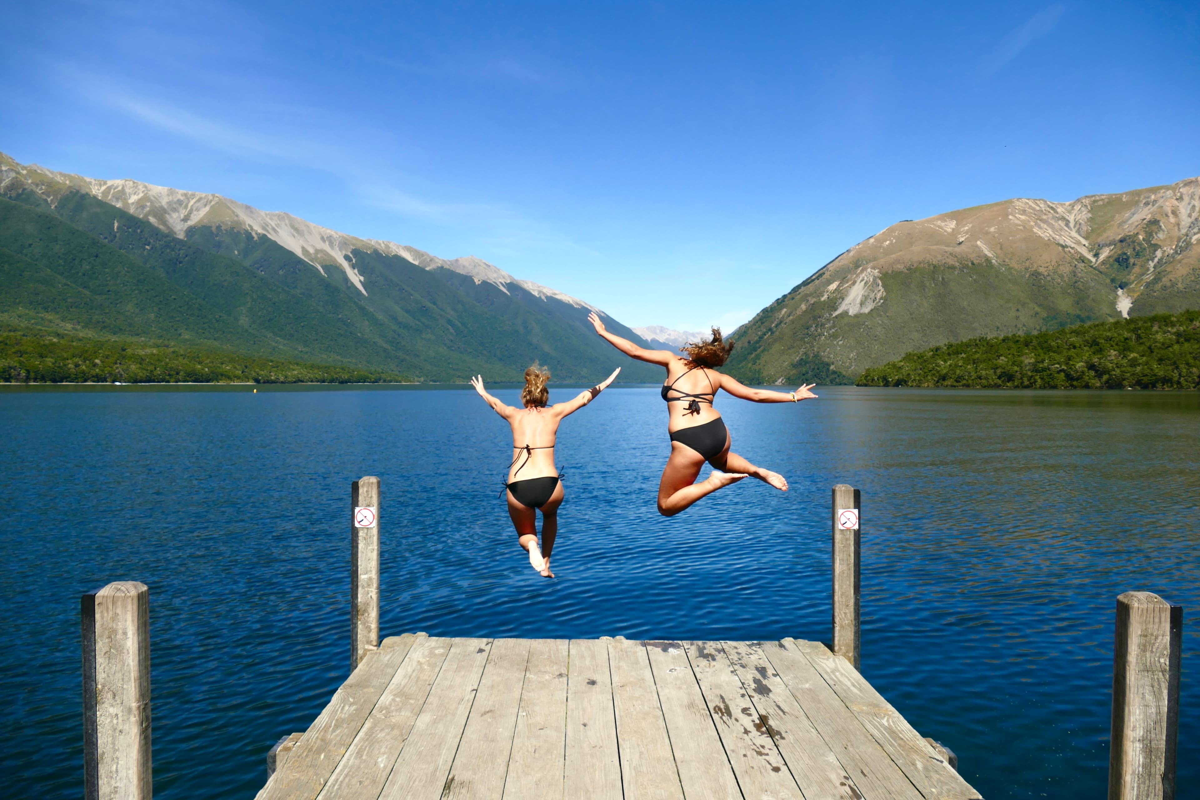 Advisor Jeannie Peters and female companion jumping into the lake from a wooden deck with mountains in view