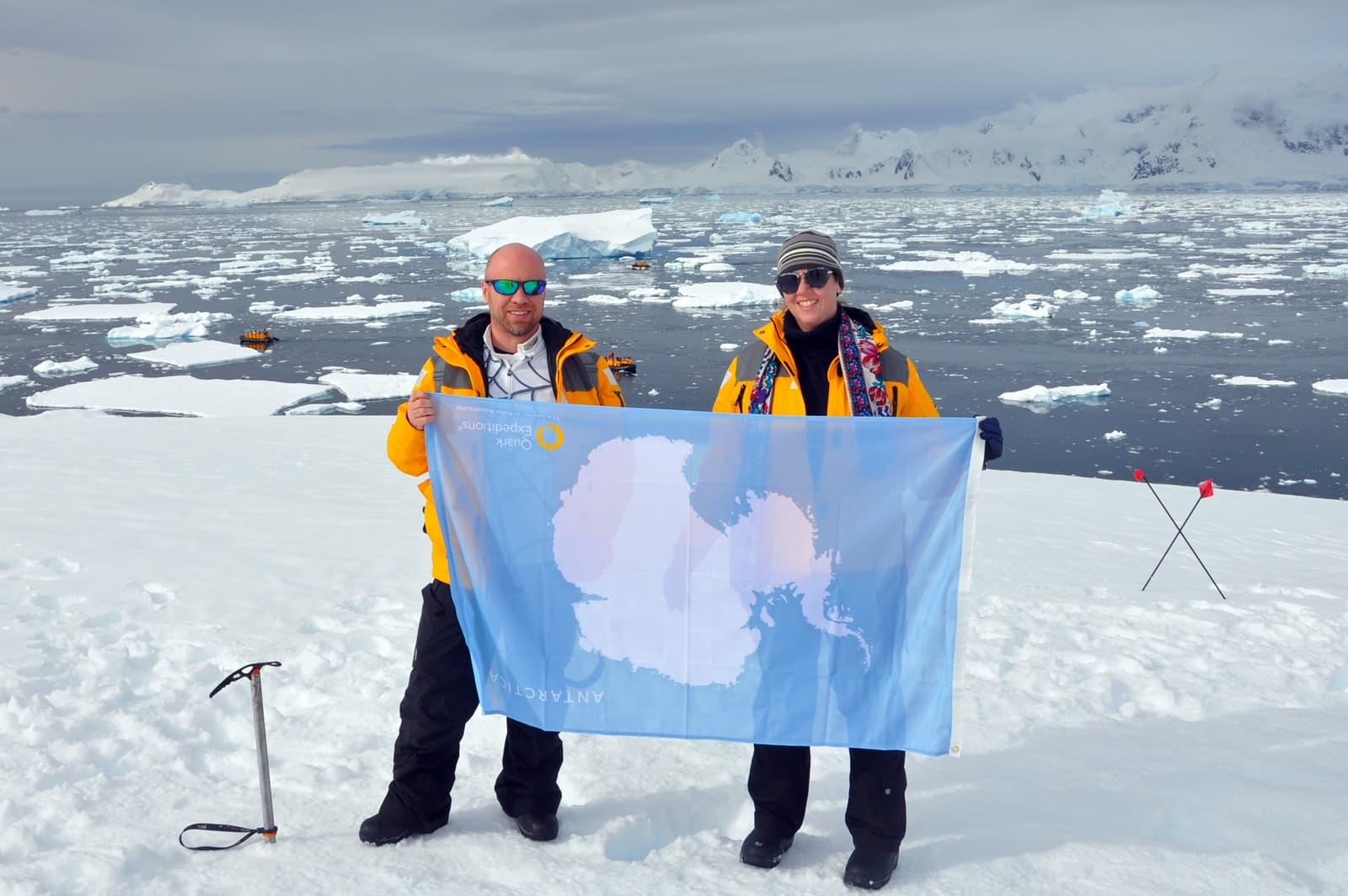 Travel advisor Tammy and male companion in yellow jackets holding a flag in the snow in Antarctica