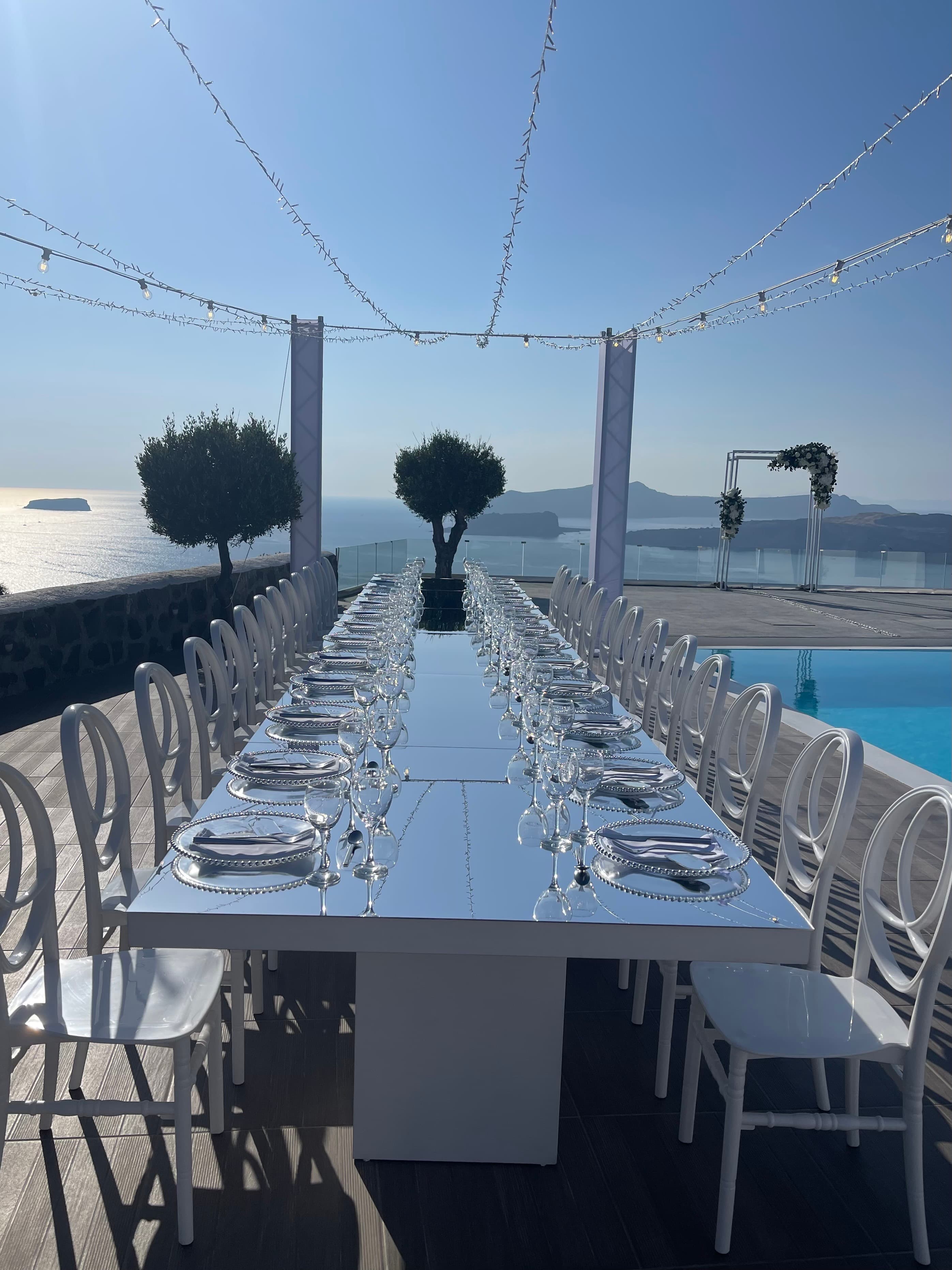 A long, elegant table set up on a pool deck overlooking the sea with string lights overhead.