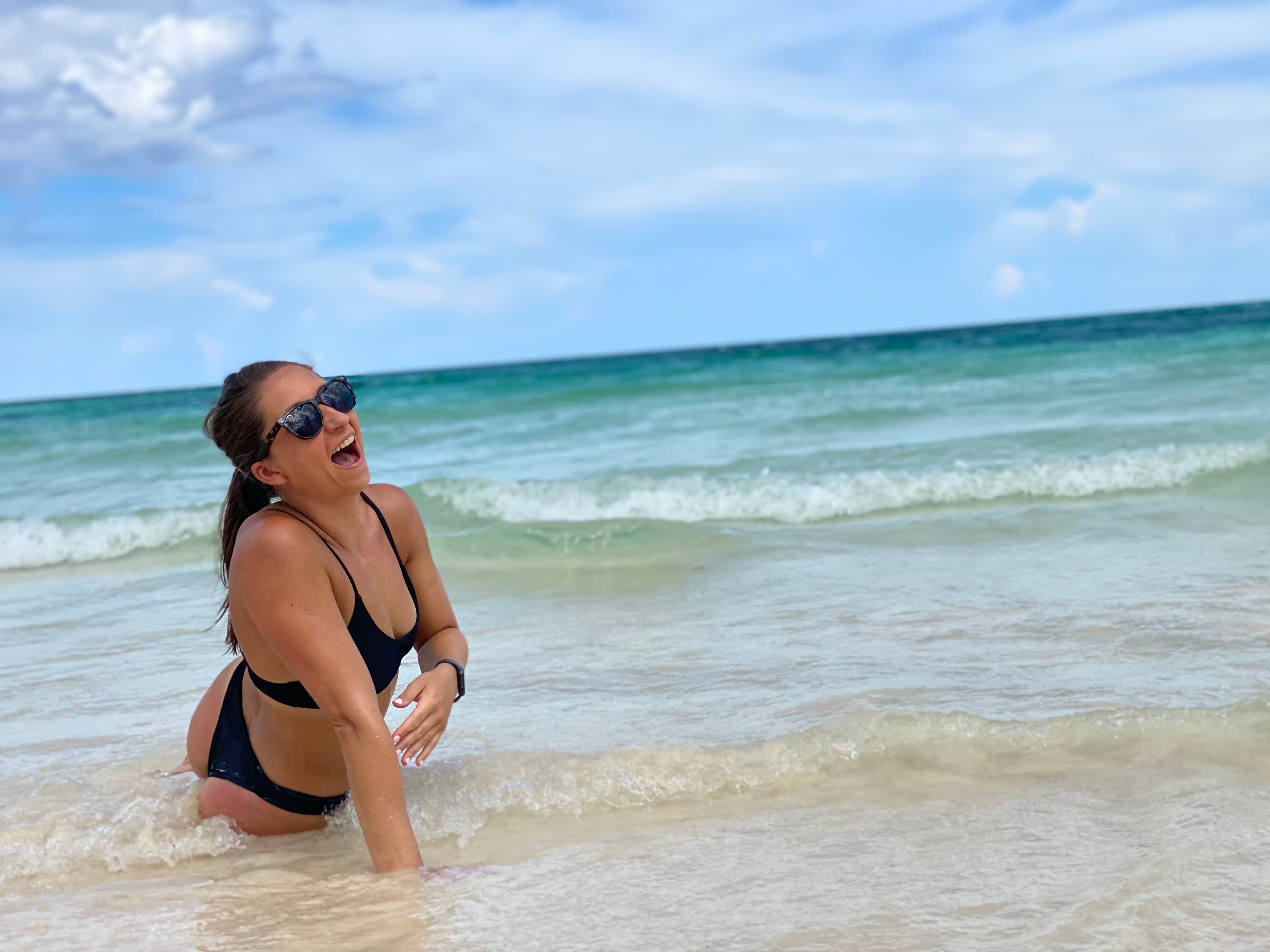 Travel advisor Sarah in black bikini sitting at the ocean shore