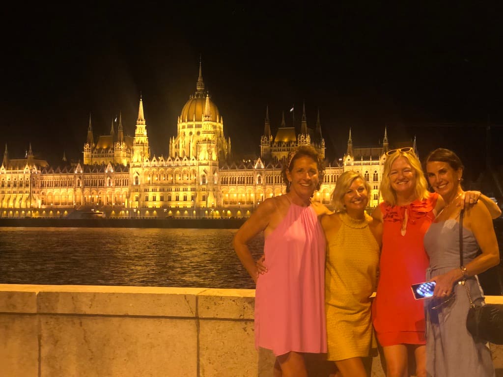 Travel advisor Kristin Rotter and three female companions posing for a group photo in Budapest in front of the river with lit-up building in the background