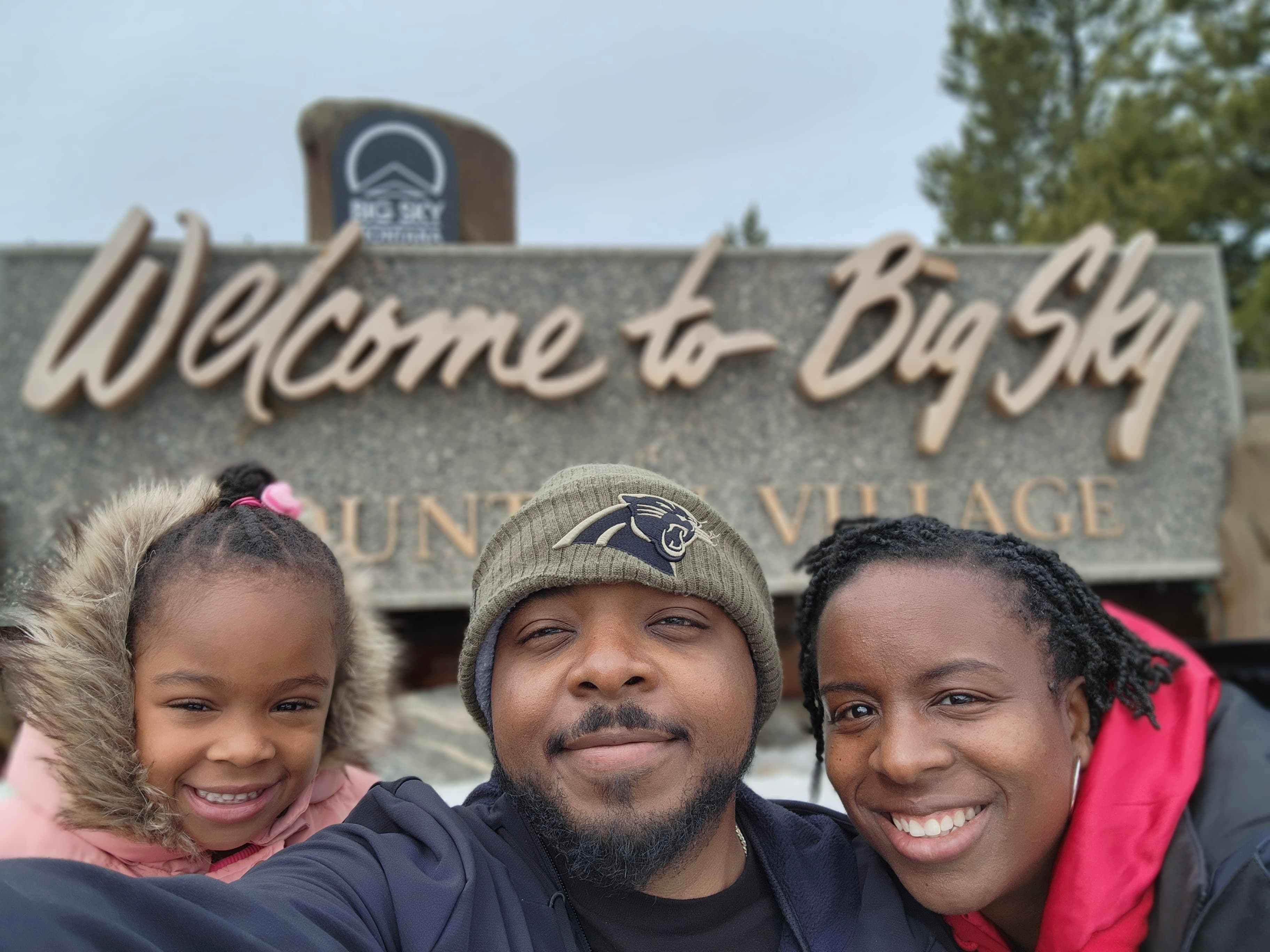 Picture of Harold with a woman and a child in front of a sign reading "Welcome to Big Sky".