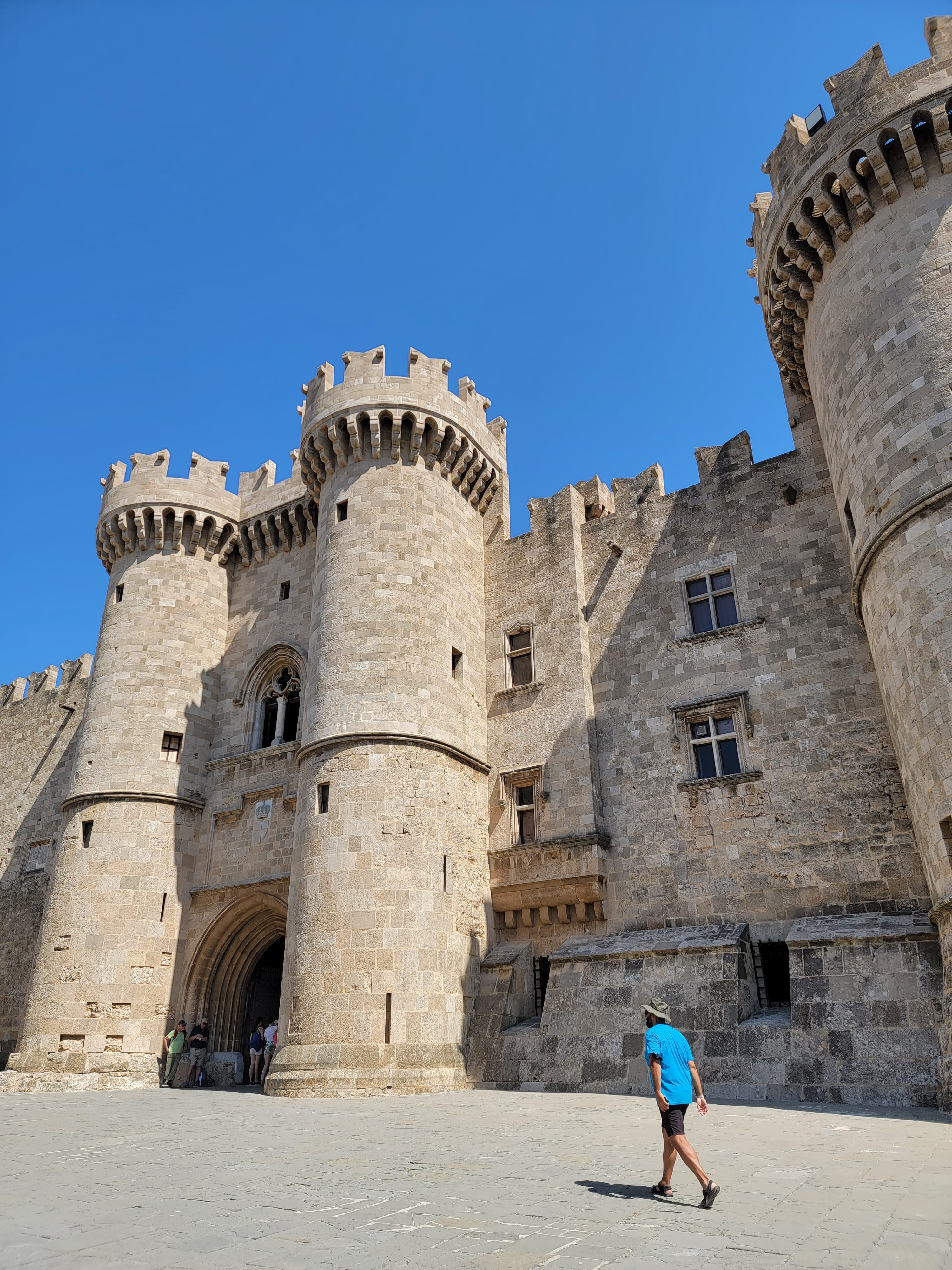 A stone castle with a person wearing shorts and a bright blue t-shirt walking in front of it.