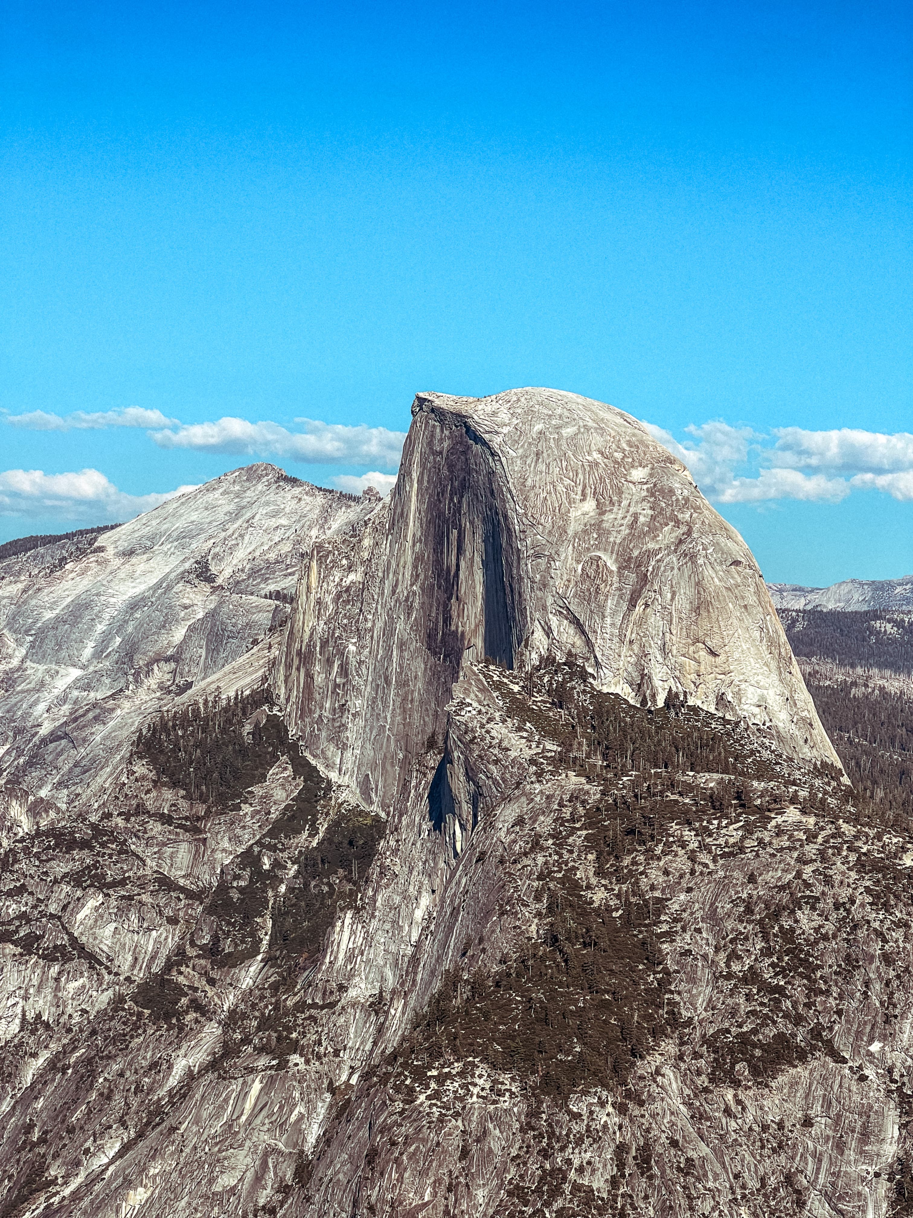 A view of the rocky terrain and peaks of Yosemite National Park with a cloudy blue sky in the background.