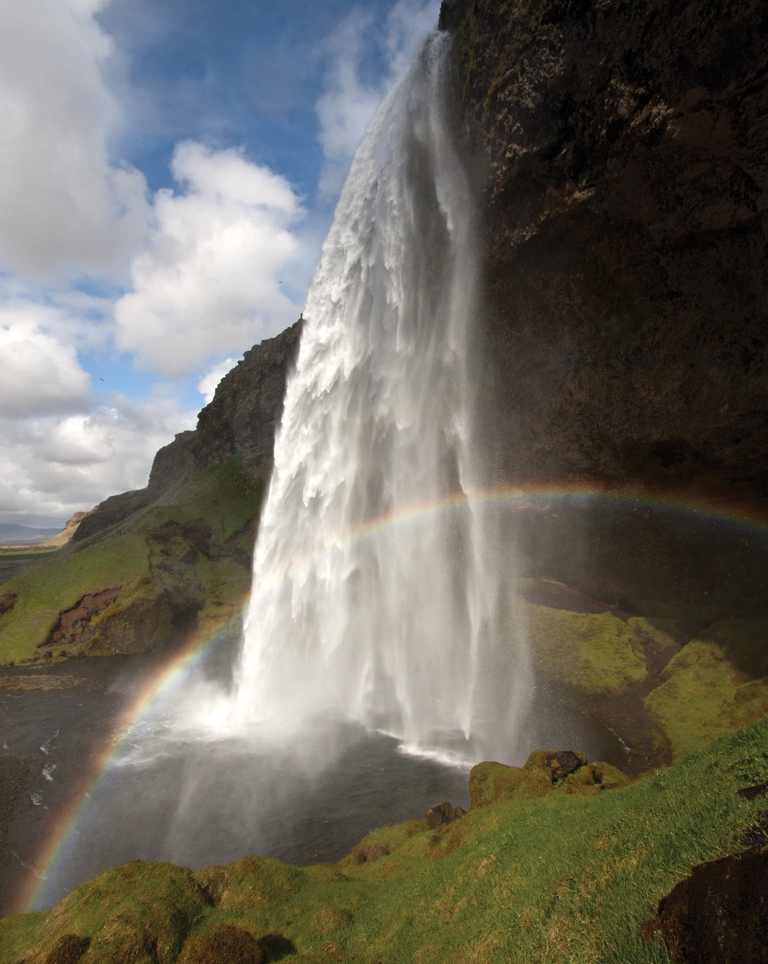 A beautiful waterfall at a mountain range with a lovely rainbow.