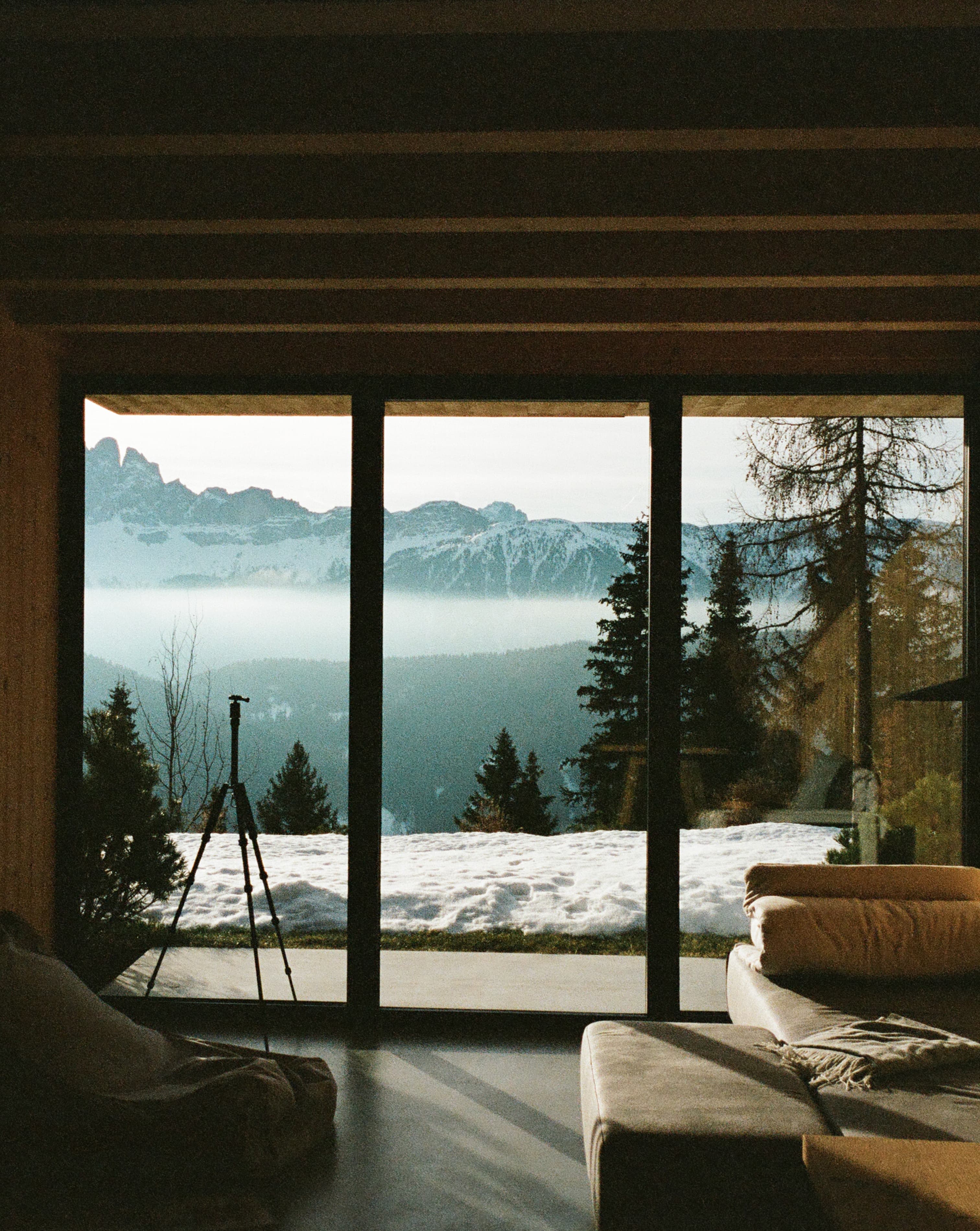 A beautiful window view of a rustic space with the snowy outdoors in the distance with mountains and a quaint forest in the distance.