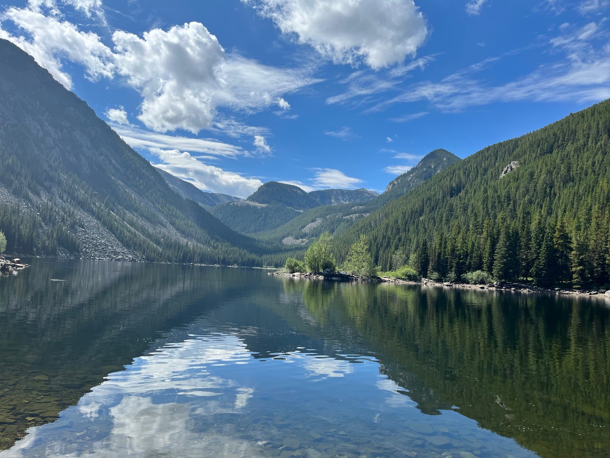 A beautiful view of a quiet body of water surrounded by mountains and a forest.