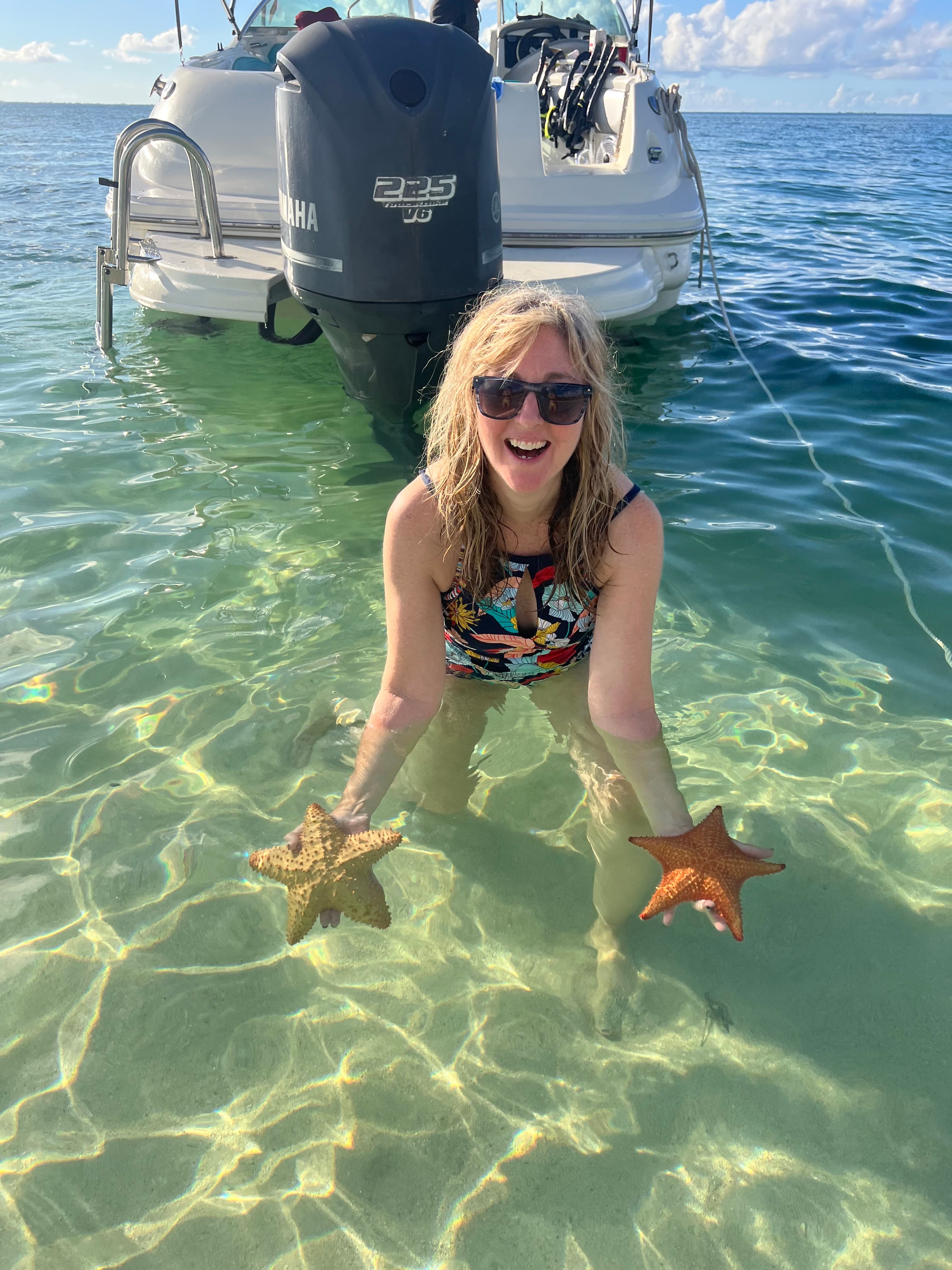 Wendy in the ocean holding two starfish from the sea before releasing them into the wild.