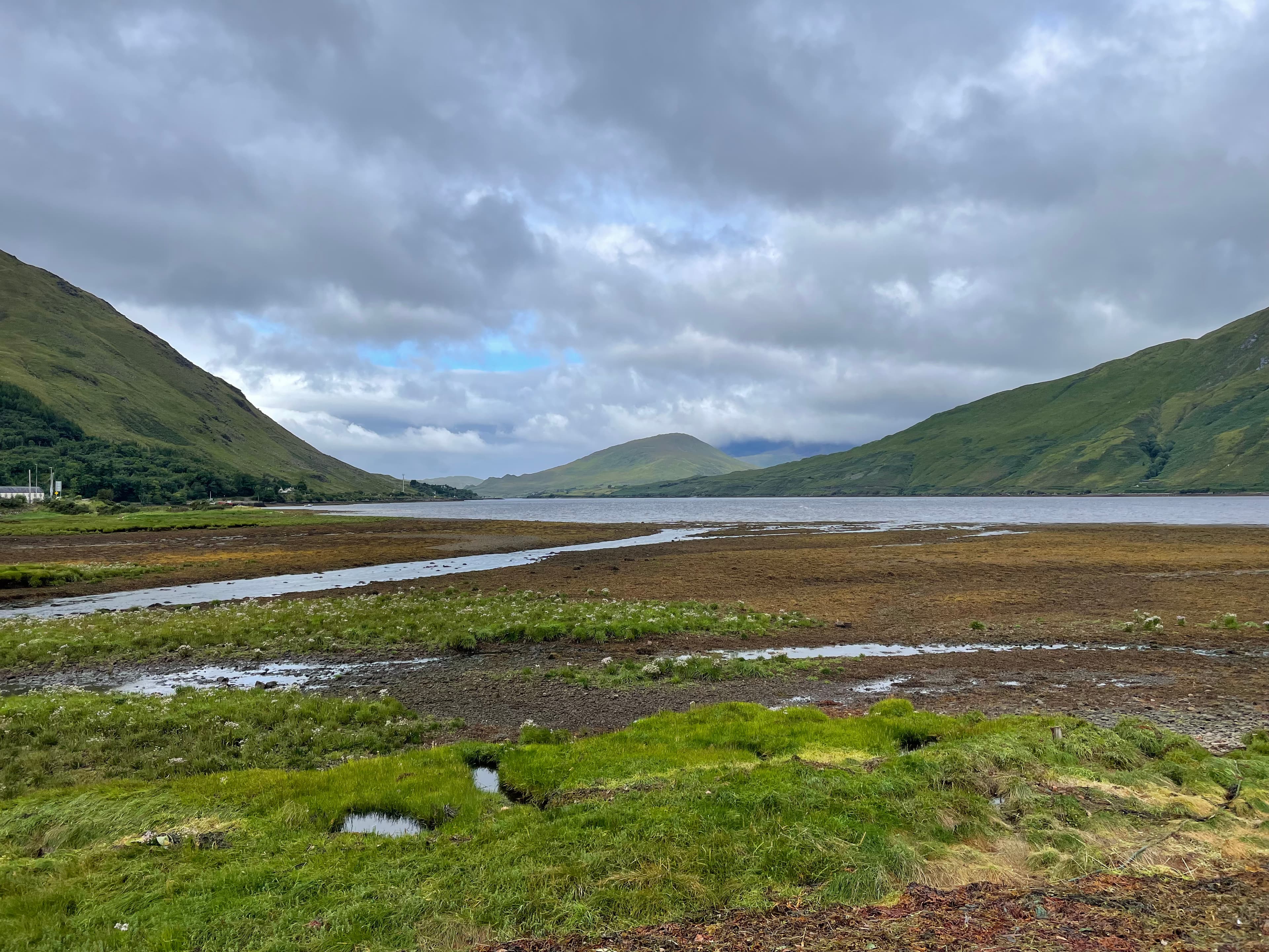 A grassy field in front of water with hills on either side on a cloudy day