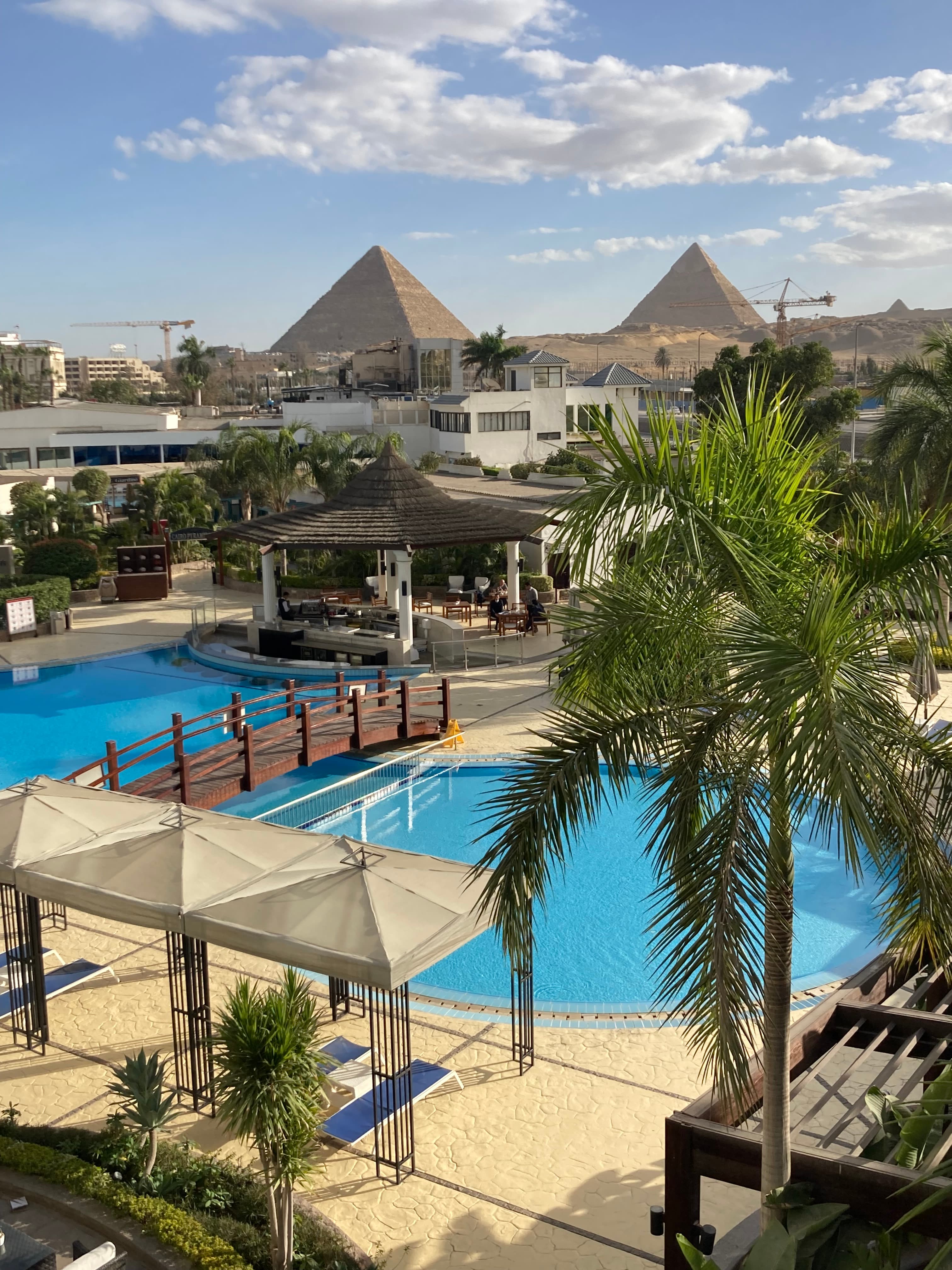 A resort with pyramids in the distance and a pool and palm trees.