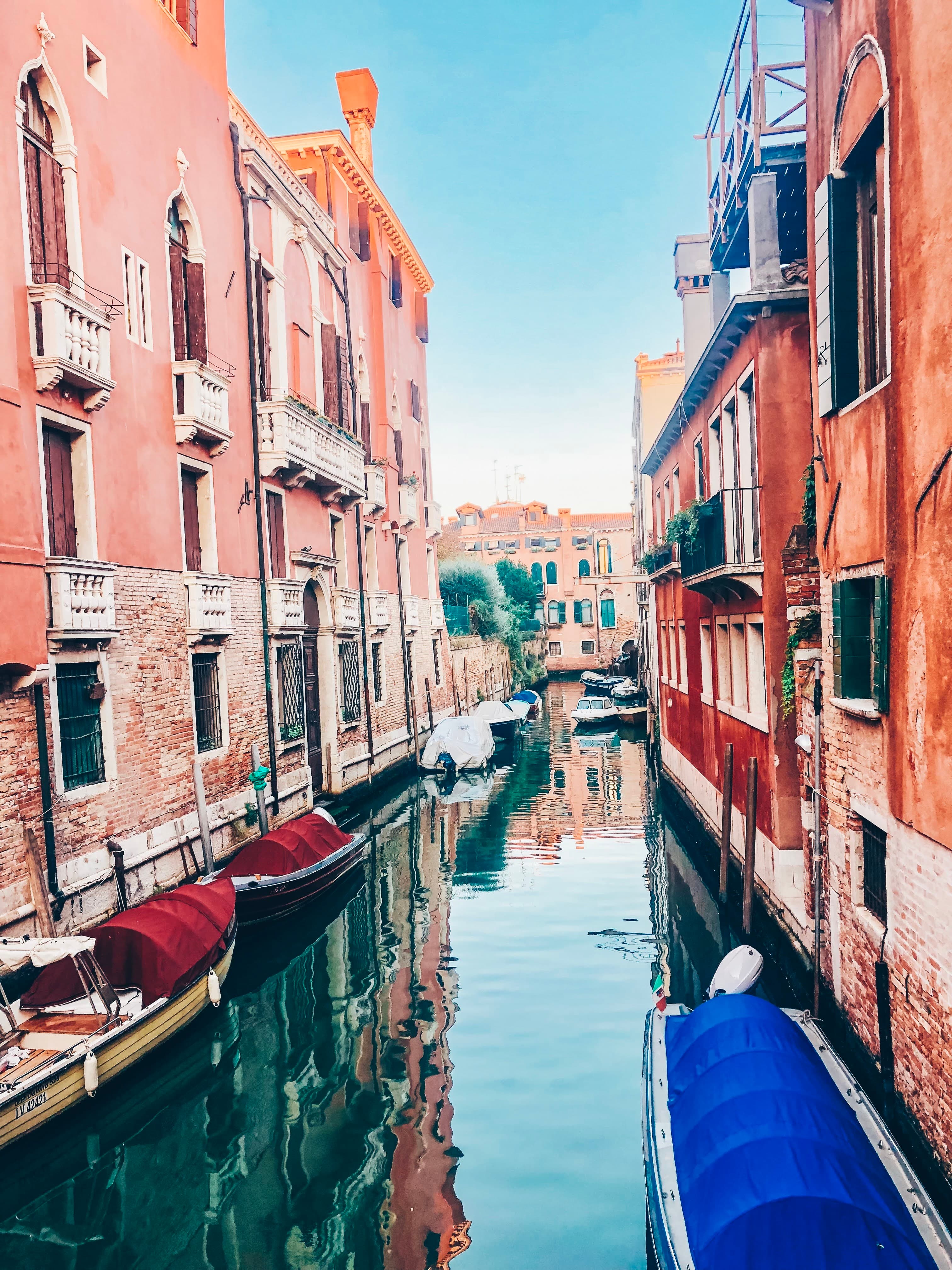 A beautiful canal with coral colored architecture and small boats docked along the buildings edge.