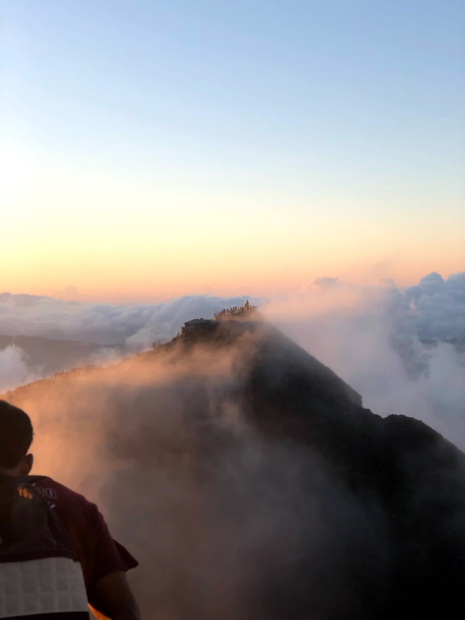A high up view of a mountain range with a colorful hues of the sun, clouds and a light layer of fog rolling in.