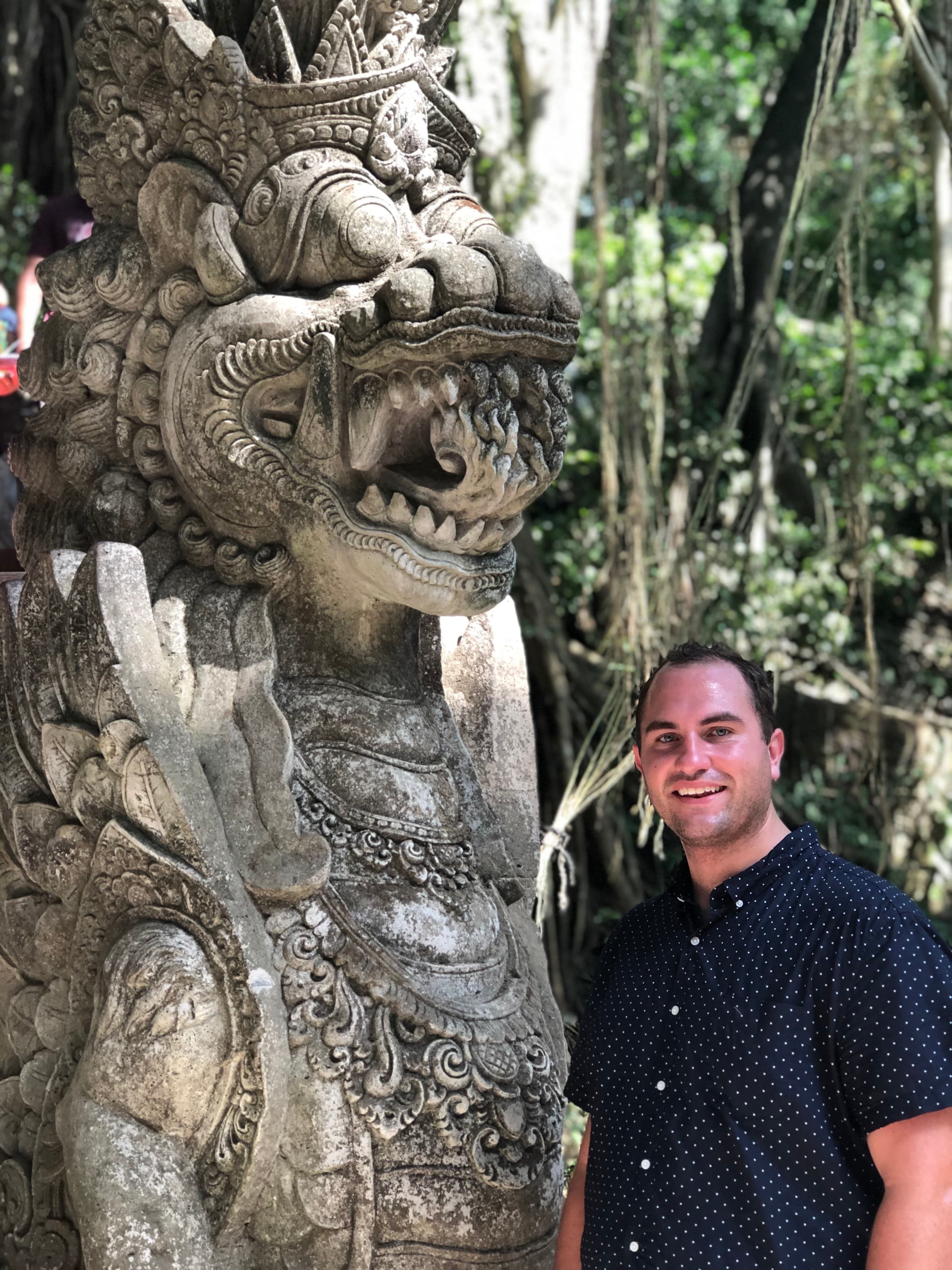 Nicholas posing next to a stone statue in the jungle.