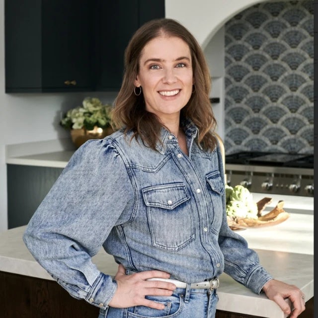 Travel Advisor Amy Shamus poses with her hand on her hip wearing a denim top and jeans in a kitchen