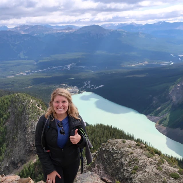 Travel advisor Kirsten Johansson stands on top of a mountain overlooking a scenic lake.