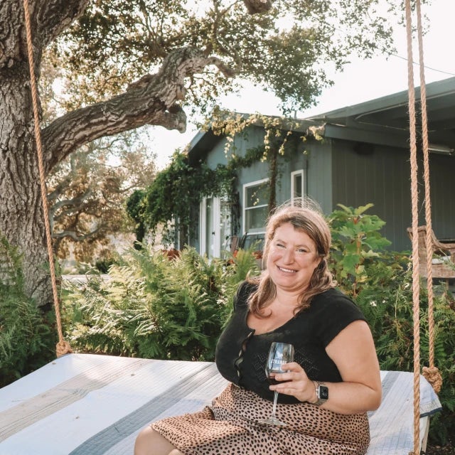 Travel advisor Rachel Kantrowitz sits on a large swing holding a wine glass.