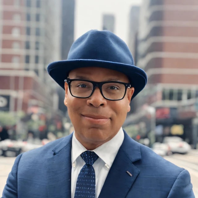 Fora travel agent Irving Macario wearing hat and glasses with a city in background.