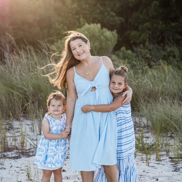 women wearing white dress standing next to two kids on sandy beach