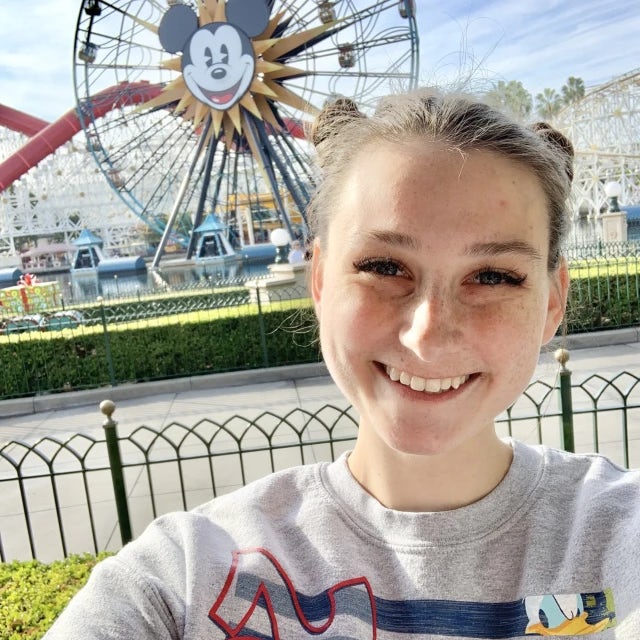 Travel Advisor Becca Stiller smiles in front of a Disney themed ferris wheel wearing a Disney sweatshirt