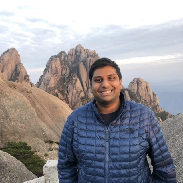 Travel Advisor Abhiram Reddy in a blue puffer jacket standing in front of large rocky mountains.