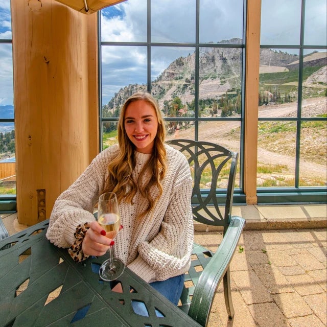 Travel Advisor Emily Duke in a white sweater holding a champagne glass with a mountain in the background.