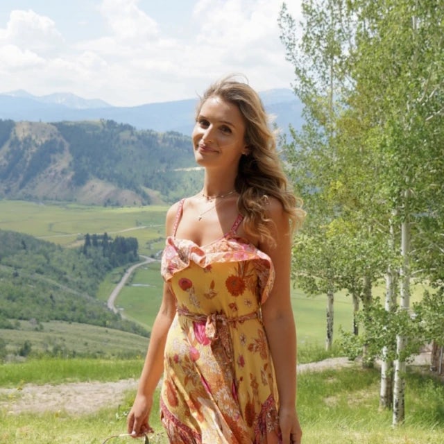 Travel Advisor Emma Cramer with a yellow floral dress and a green valley behind her.