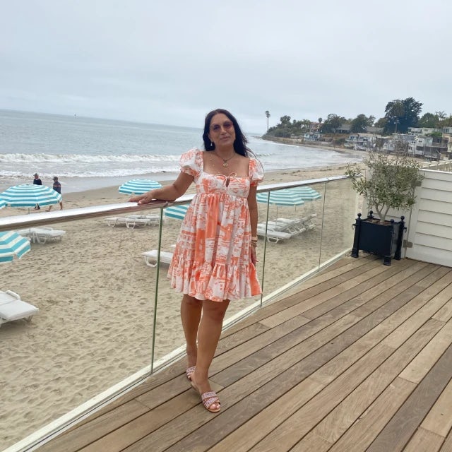 Travel Advisor Hasmik Vrtanesyan in an orange and white dress in front of a beach.