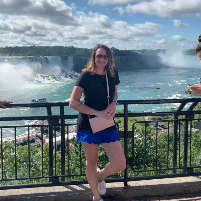 Travel Advisor Jessica Ercolano in a black shirt and blue shorts with green trees and waterfalls behind.