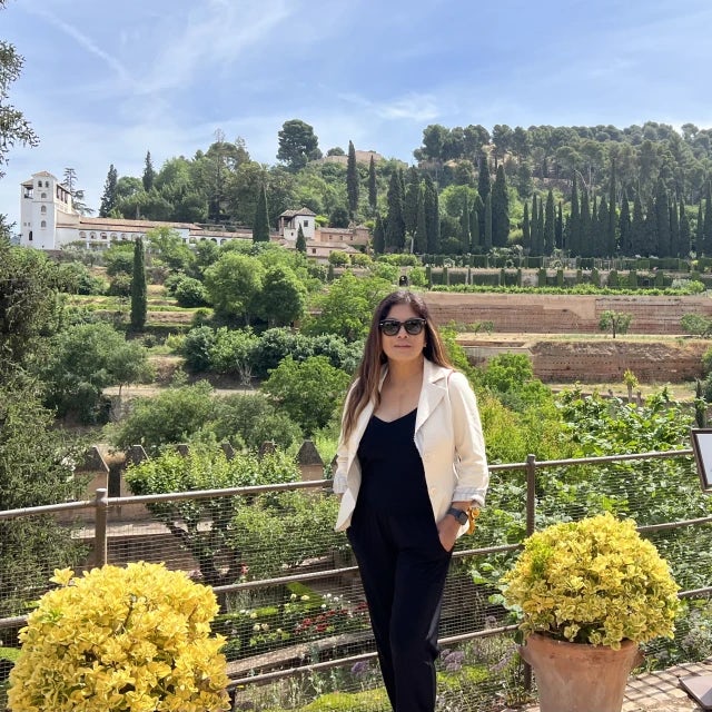 Woman wearing black pants and black top with trees and gardens in the background during daytime