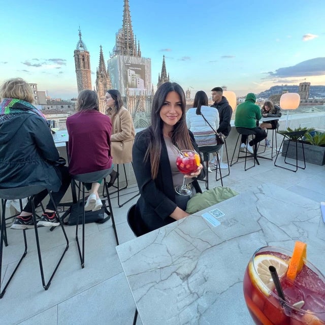 Travel Advisor Betsy Zambrano drinking a red drink on a rooftop overlooking a church.