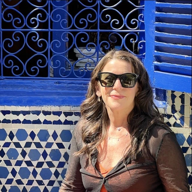 travel advisor Michelle Marx in an orange dress and a black top in front of a blue window