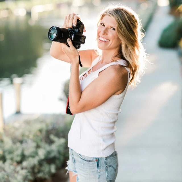 Travel Advisor Kelley Ferro with a camera in front of a lake and green bushes.