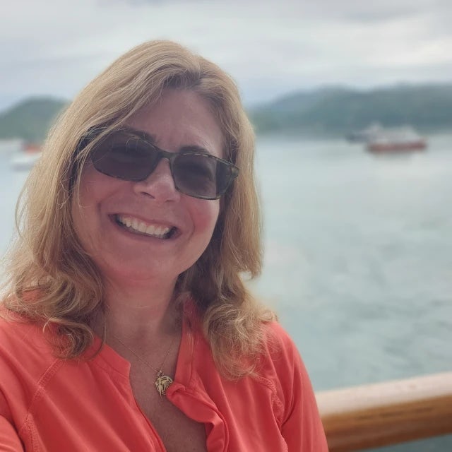 Travel Advisor Kristin Stone in an orange shirt in front of a lake with mountains and boats.