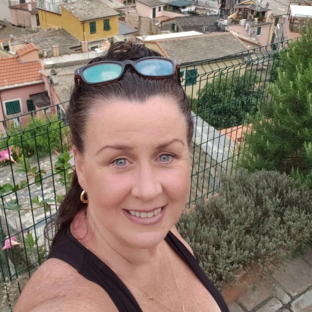 Travel Advisor Natasha Jiovino standing on a hilltop with colorful houses and the sea in the distance.