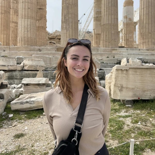 Travel Advisor Olivia Lofstad in a tan shirt with a black crossbody bag in front of ancient ruins.