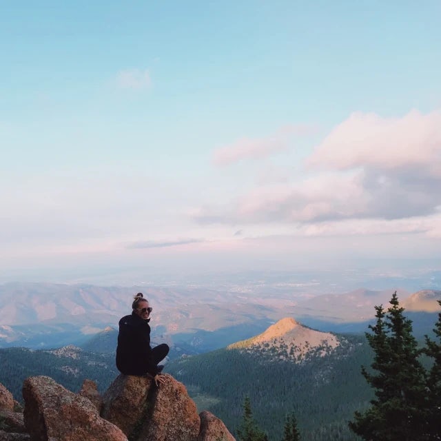 Travel Advisor Shannon Ranzini sitting on a rock at sunset with mountains in the distance.