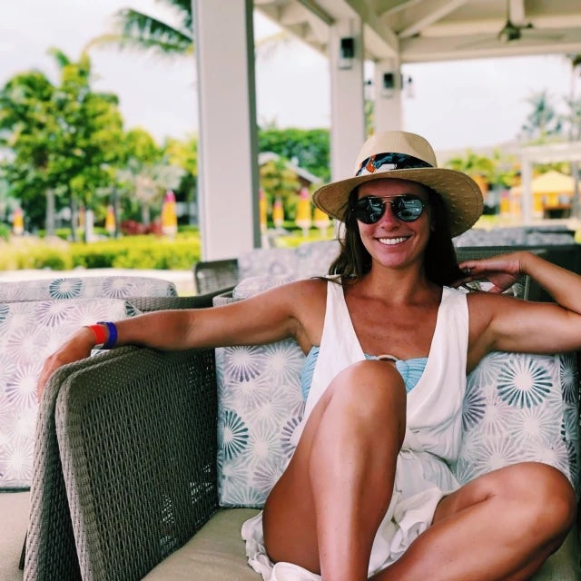 a woman in a hat and sunglasses sits on a chair in a tropical destination