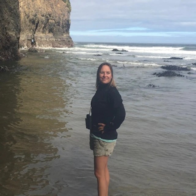 Travel Advisor Whitney Fessler in a black sweatshirt and khaki shorts standing on the beach.