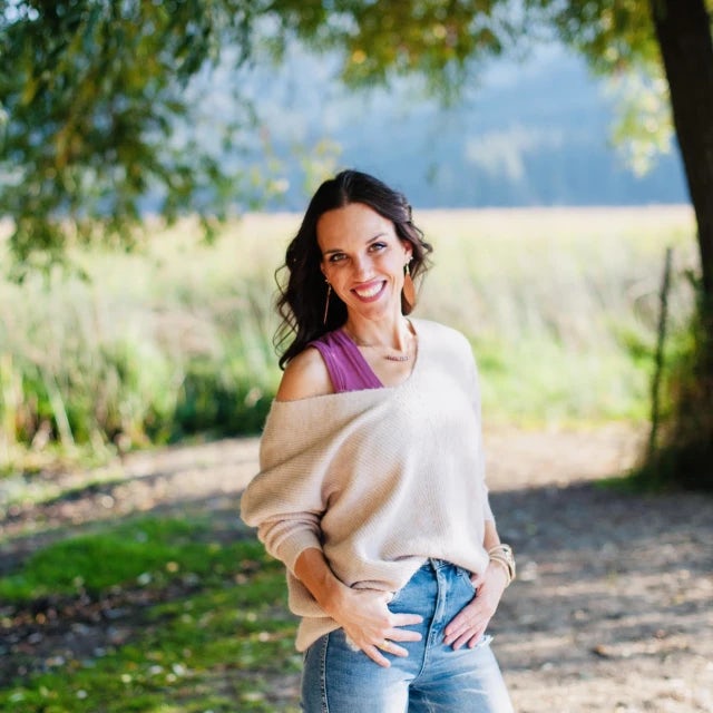 Travel Advisor Amber Tice stands in a clearing of a field under a tree wearing jeans and a sweater