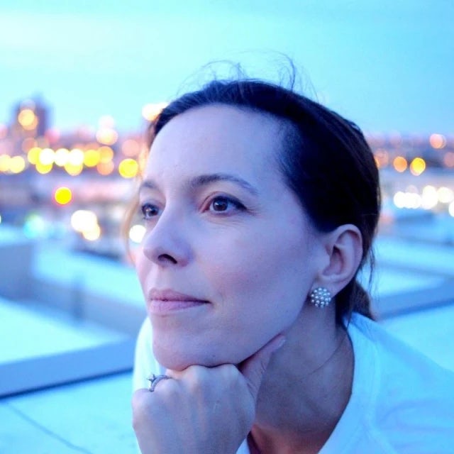 Travel Advisor Sloane Davidson looks into the distance on a rooftop with a sparkling city at sunset behind her 