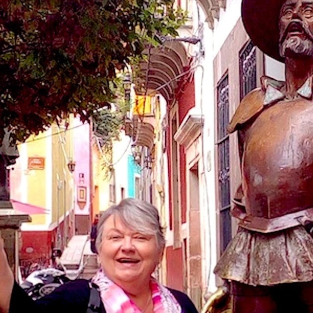 Travel Advisor Mary Manix stands next to a bronze statue on an old cit street with color buildings behind her 